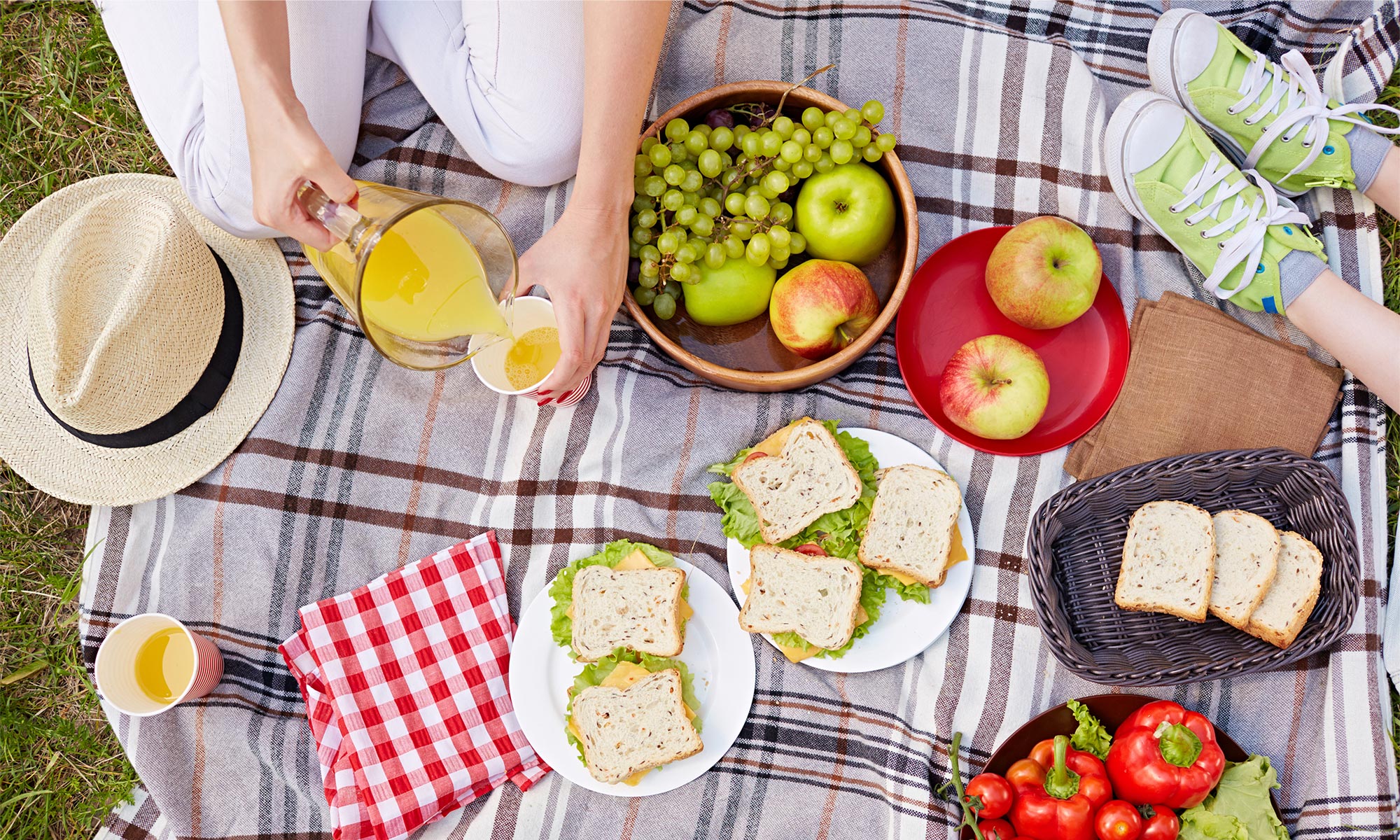 Två personer på picknik utomhus en vacker sommardag med frukt, mackor och juice