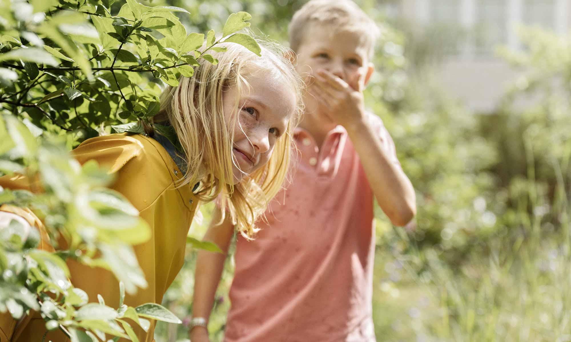 Två barn liker kurragömma ute i trädgården en solig sommardag